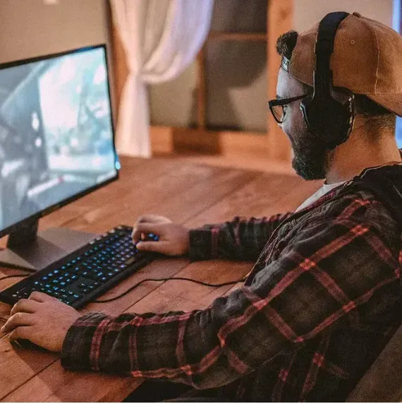 Hombre con gafas y gorra usando teclado de computadora en escritorio.