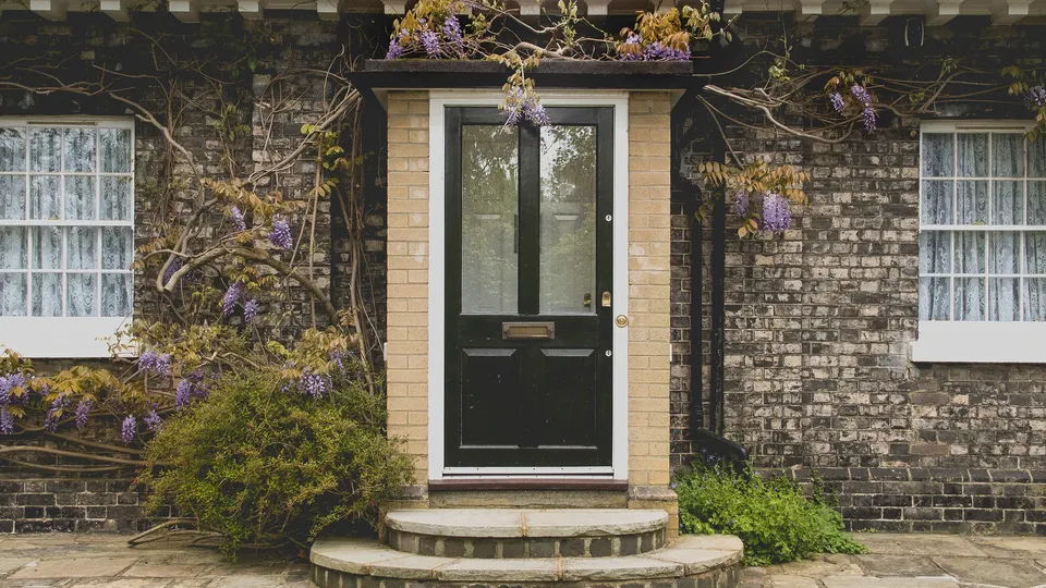 County Carlow: Black door with white frame on brick house entrance surrounded by purple wisteria flowers.