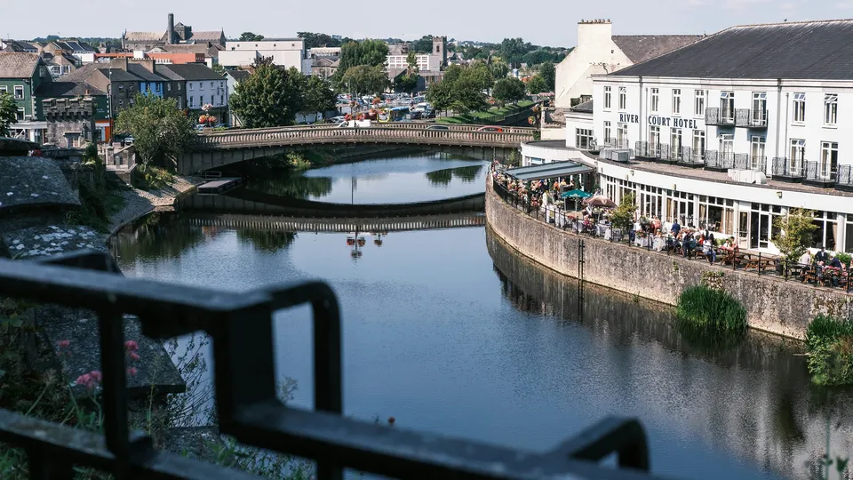 Solar panel installations. County Kilkenny: River with bridge and waterfront hotel terrace with diners.