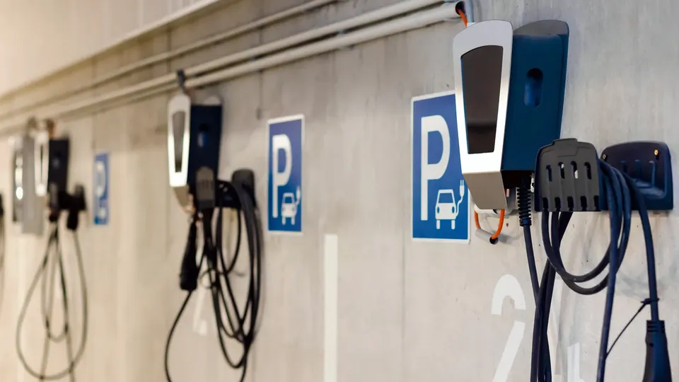 Row of electric vehicle charging stations mounted on wall with cables.