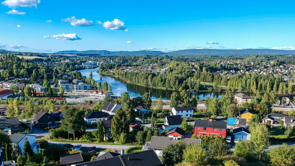 Luftfoto av elvestad med fargede hus, elv og skogkledde åser.