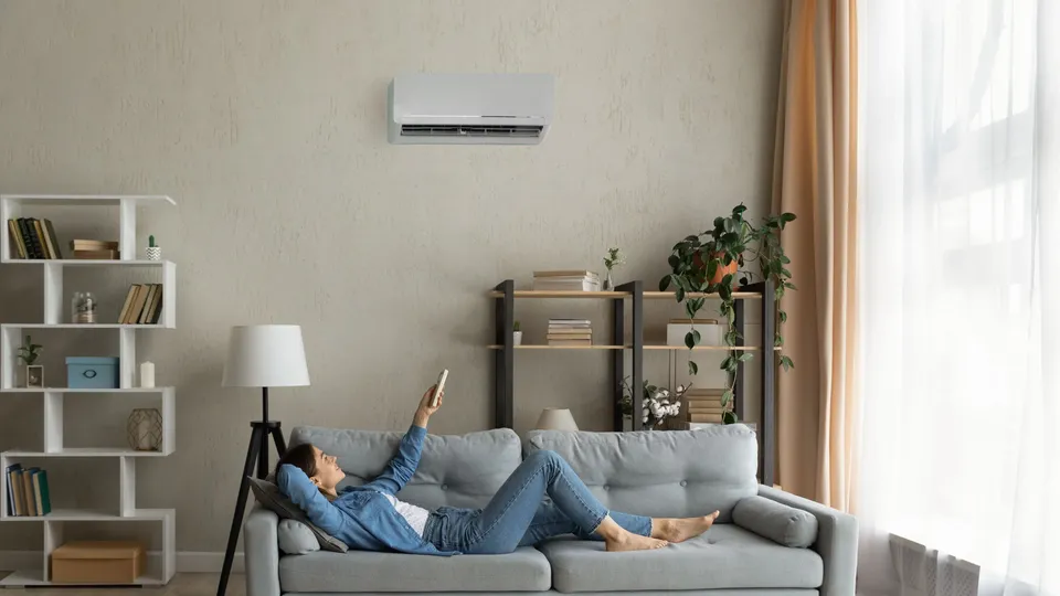 Persona sdraiata sul divano con il braccio sollevato verso l'unità di climatizzazione a parete.