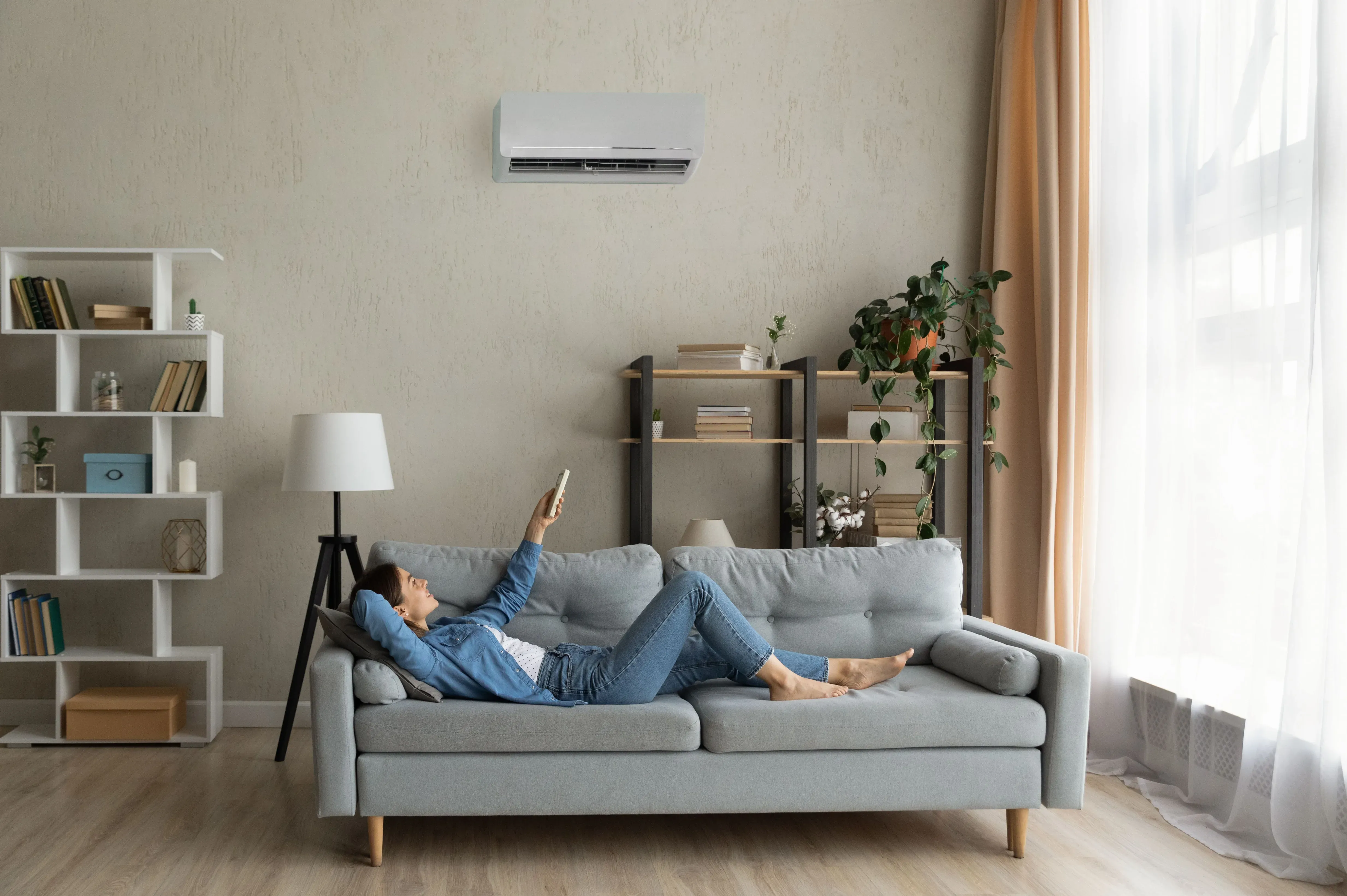 Persona sdraiata sul divano con il braccio sollevato verso l'unità di climatizzazione a parete.