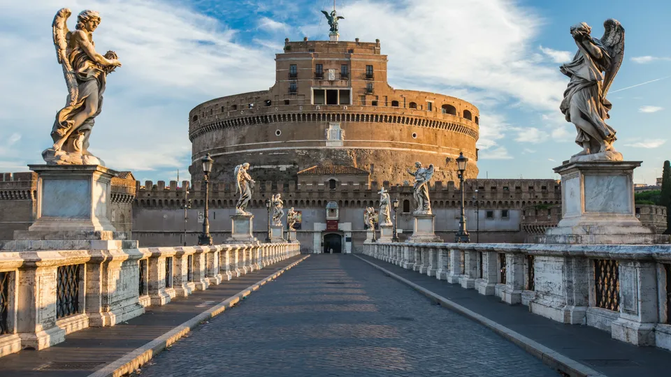 Ponte che conduce a una torre fortezza storica con statue di angeli sui parapetti.