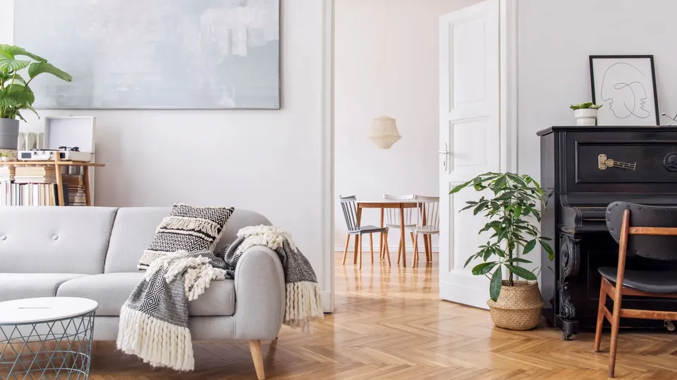 Ljust vardagsrum med grå soffa, träinredning och ett svart piano.