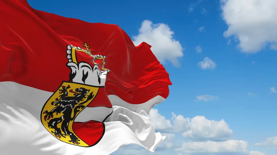 Rot-weiße Flagge Salzburgs mit dem Salzburger Wappen vor blauem Himmel mit Wolken.