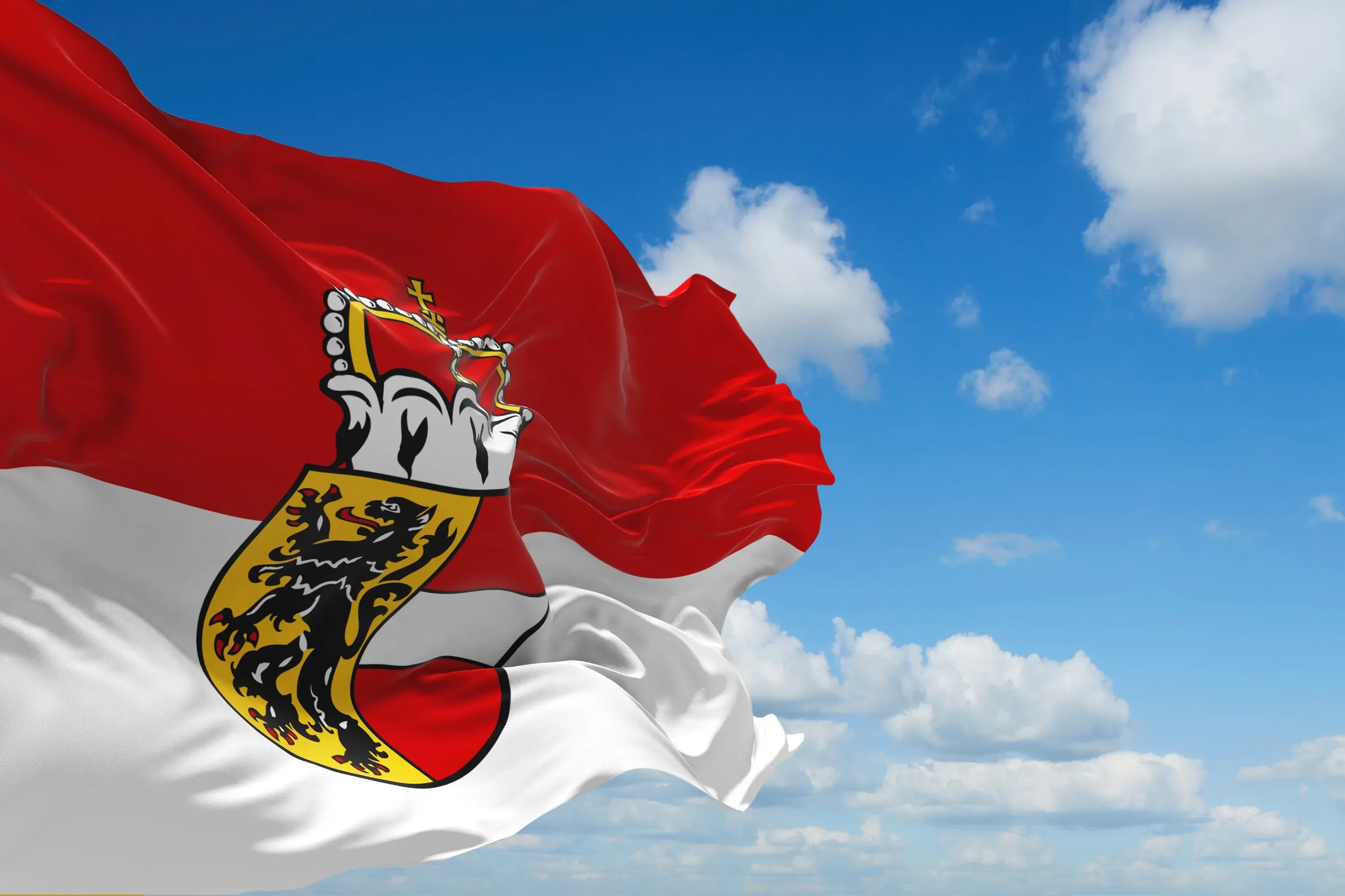 Rot-weiße Flagge Salzburgs mit dem Salzburger Wappen vor blauem Himmel mit Wolken.