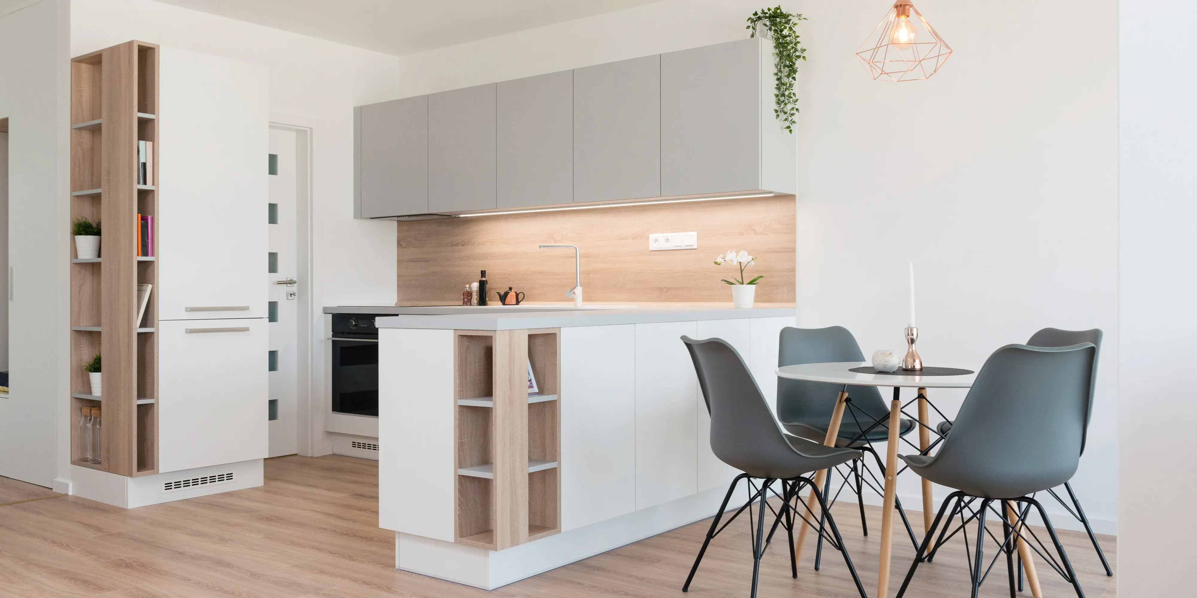 Moderne kjøkken med grå skap, tredetaljer og spisebordet med grå stoler.