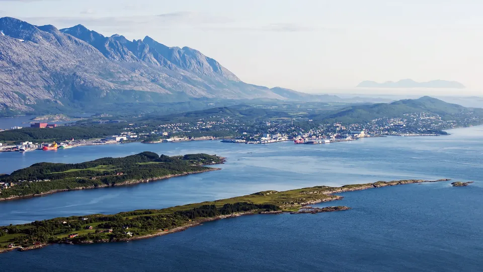 Luftfoto av kystby med havn, øyer og snødekte fjellkjede.