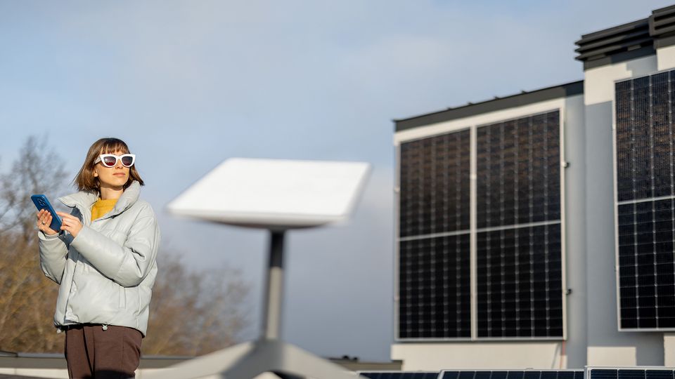 Bilde av en antenne til satellittbredbånd i forgrunnen med en kvinne som står i bakgrunnen og ser til siden.