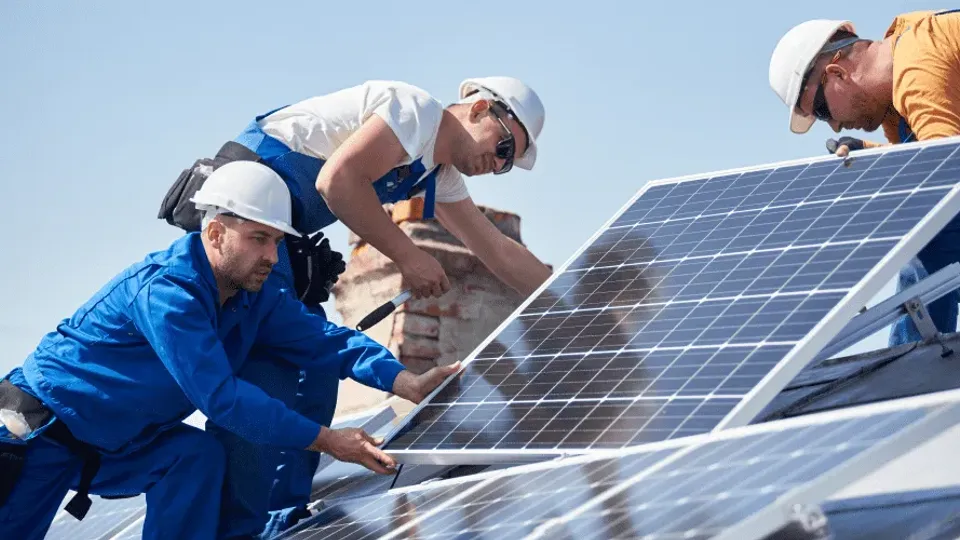 Three workers installing solar panels on a roof.