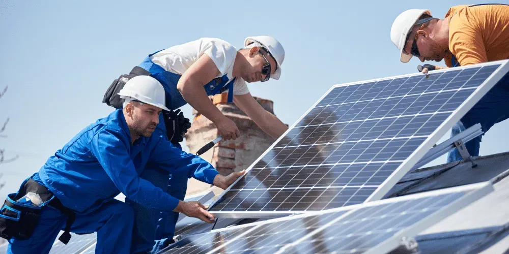 Three workers installing solar panels on a roof.
