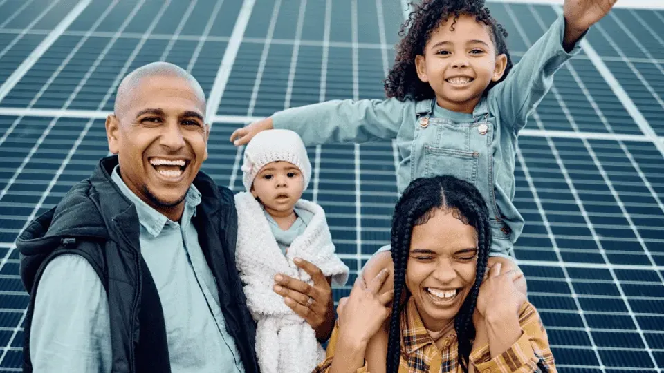 Family of four smiling in front of solar panels.