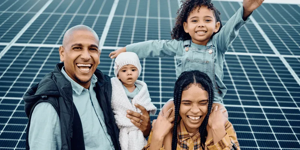 Family of four smiling in front of solar panels.