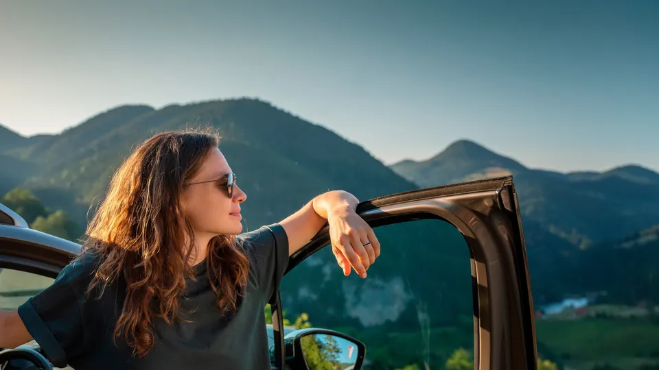 Mujer asomándose por la ventana del coche contemplando el paisaje montañoso.