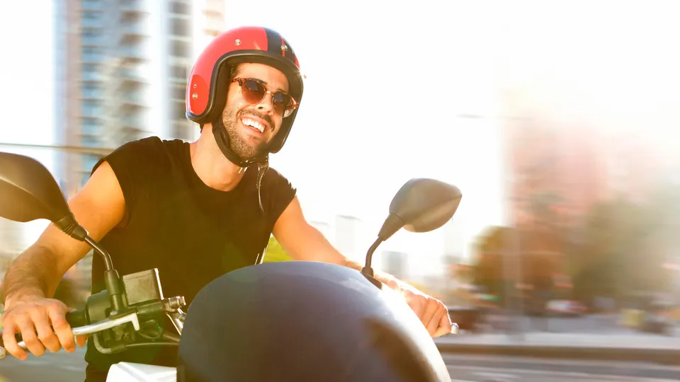 Hombre montando una motocicleta usando casco rojo y gafas de sol.