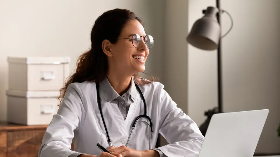 Doctora sonriendo frente a laptop en oficina.