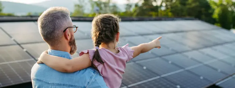Un uomo tiene in braccio una bambina che indica le file di pannelli solari su un tetto.