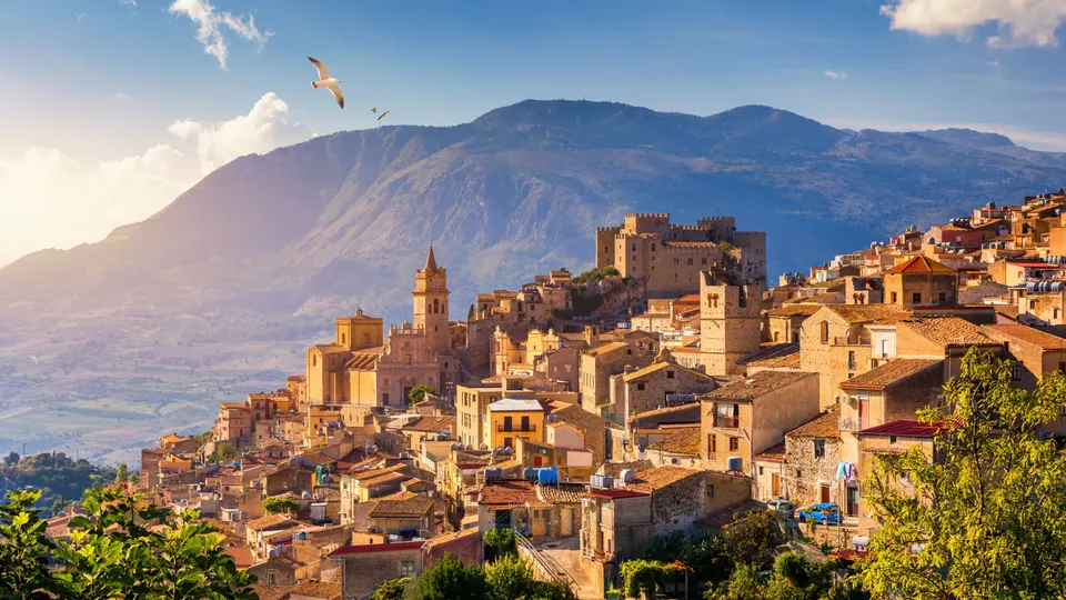 Borgo medievale su collina con castello e chiesa che dominano la valle montana.
