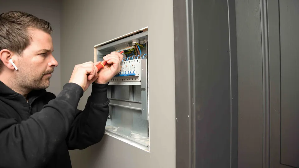 Elektriker arbeider med automatsikringer og ledninger i et sikringsskap.