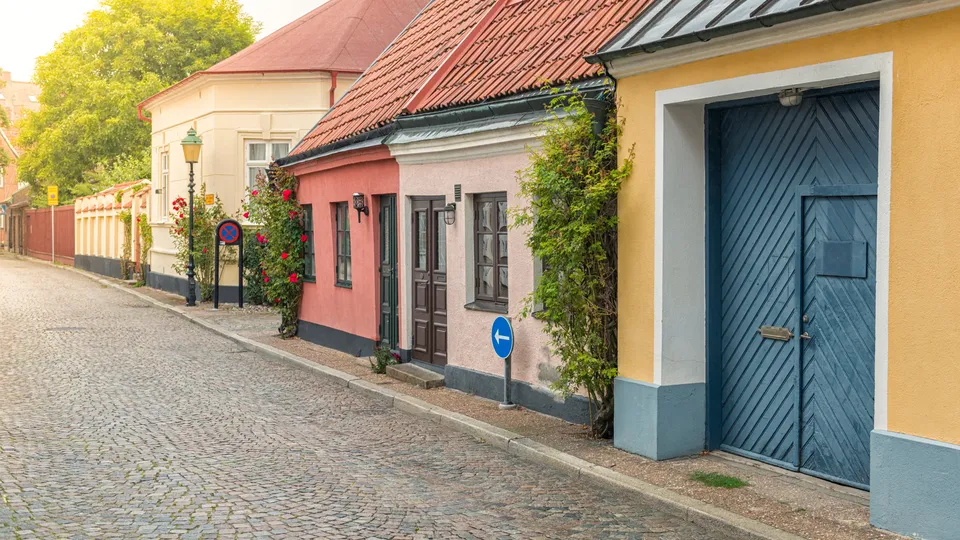 Färgglada radhus längs en kullerstensgata i Ystad med murklädda växter och blommor.