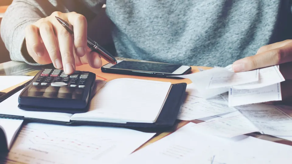 Person använder miniräknare och penna medan hen granskar finansiella dokument och gör anteckningar.