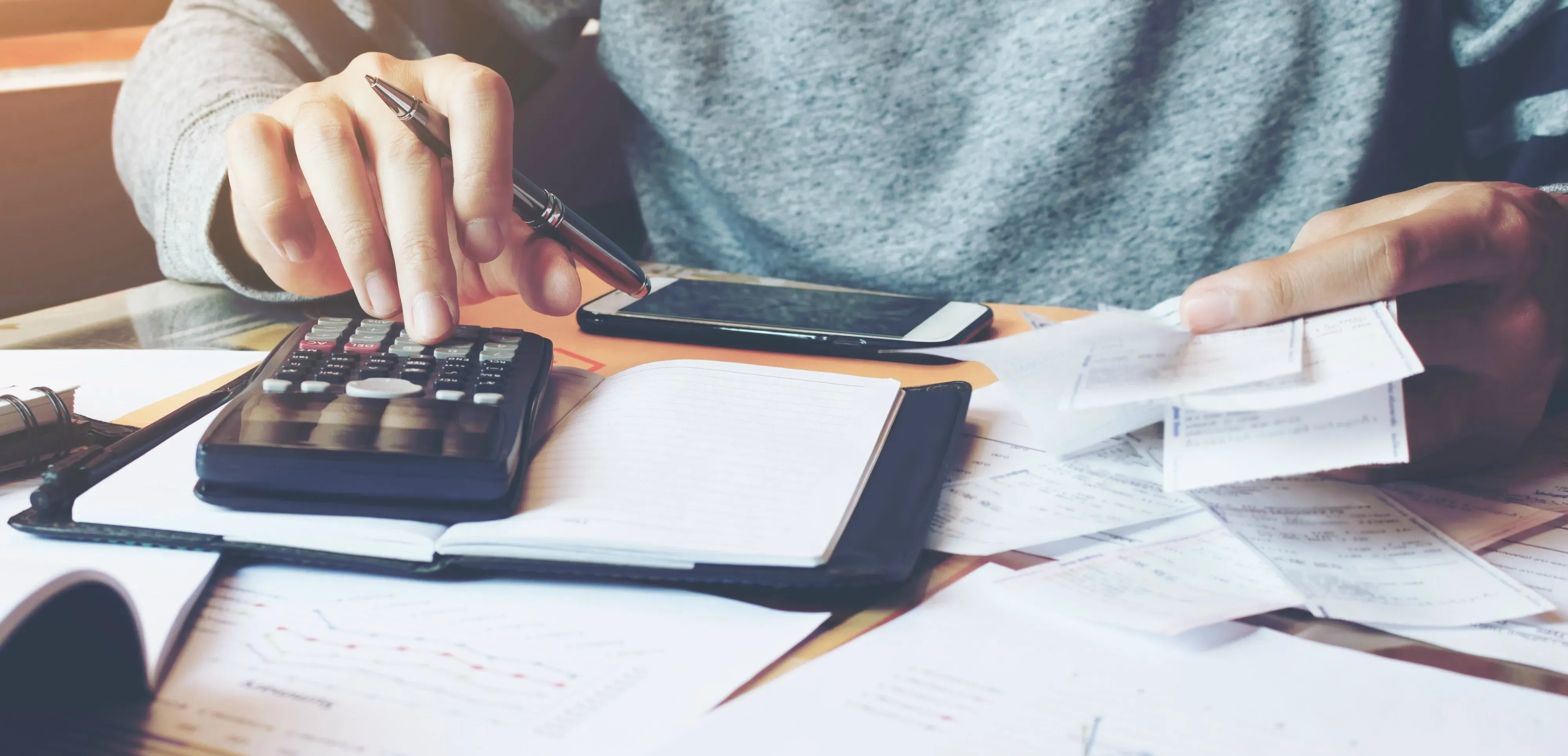 Person använder miniräknare och penna medan hen granskar finansiella dokument och gör anteckningar.
