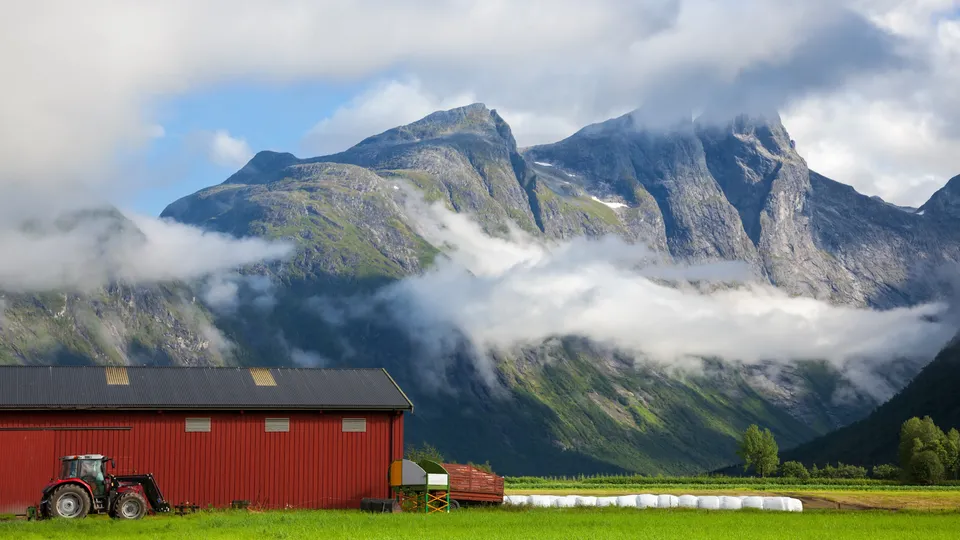Rød låve med traktor og jordbruksutstyr i fjelldale.