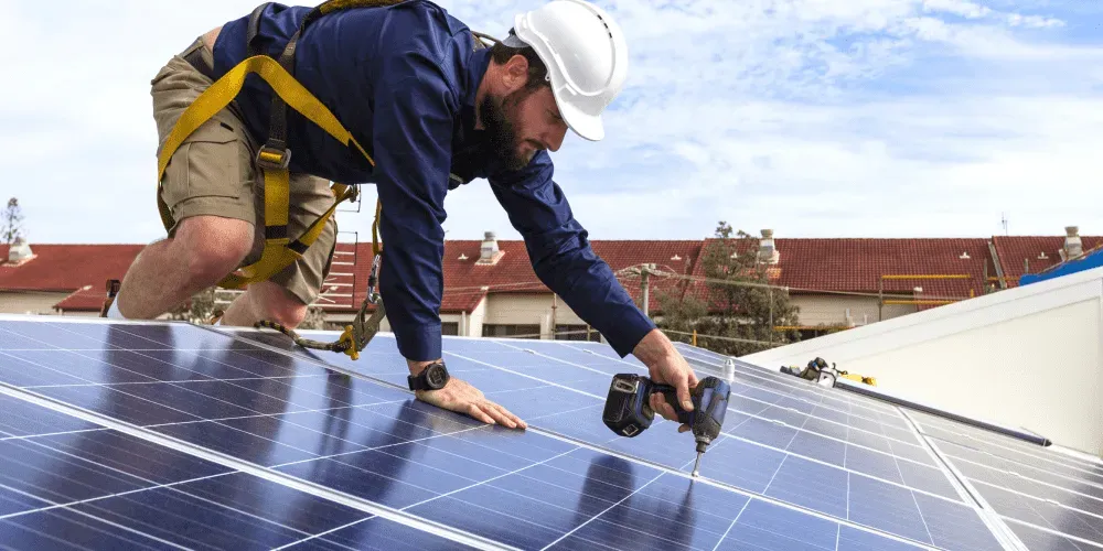 Worker installing solar panels on rooftop using power drill.