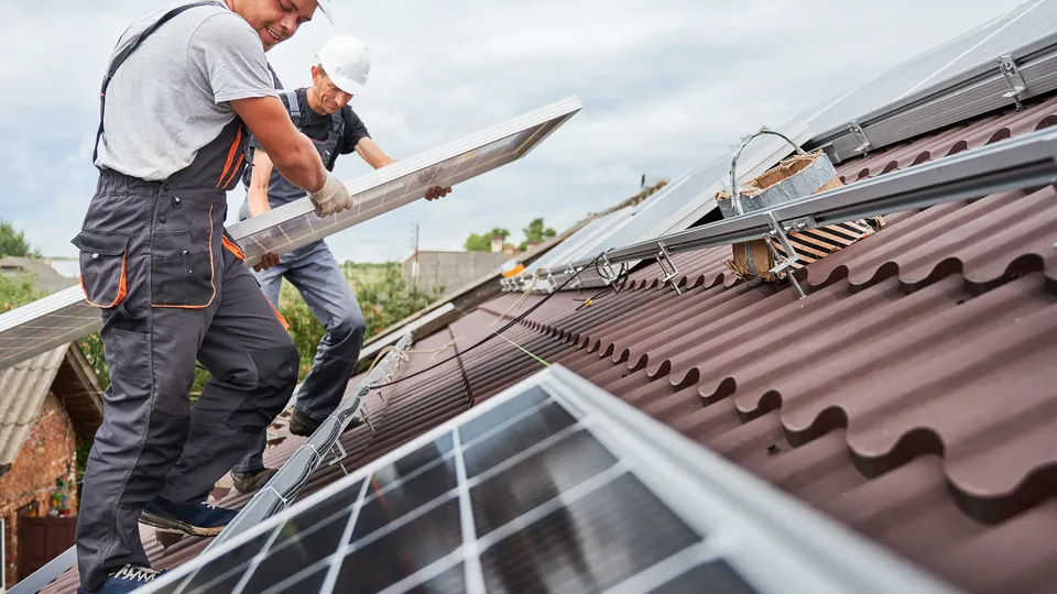 Zwei Monteure installieren Photovoltaikmodule auf einem Hausdach.