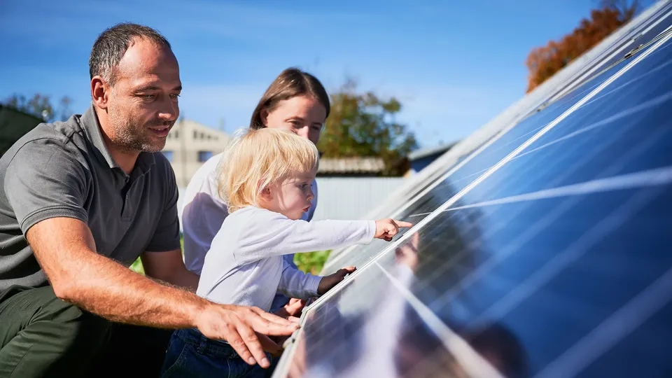 Familie mit kleinem Kind betrachtet Solarmodule einer Photovoltaikanlage an einem sonnigen Tag.
