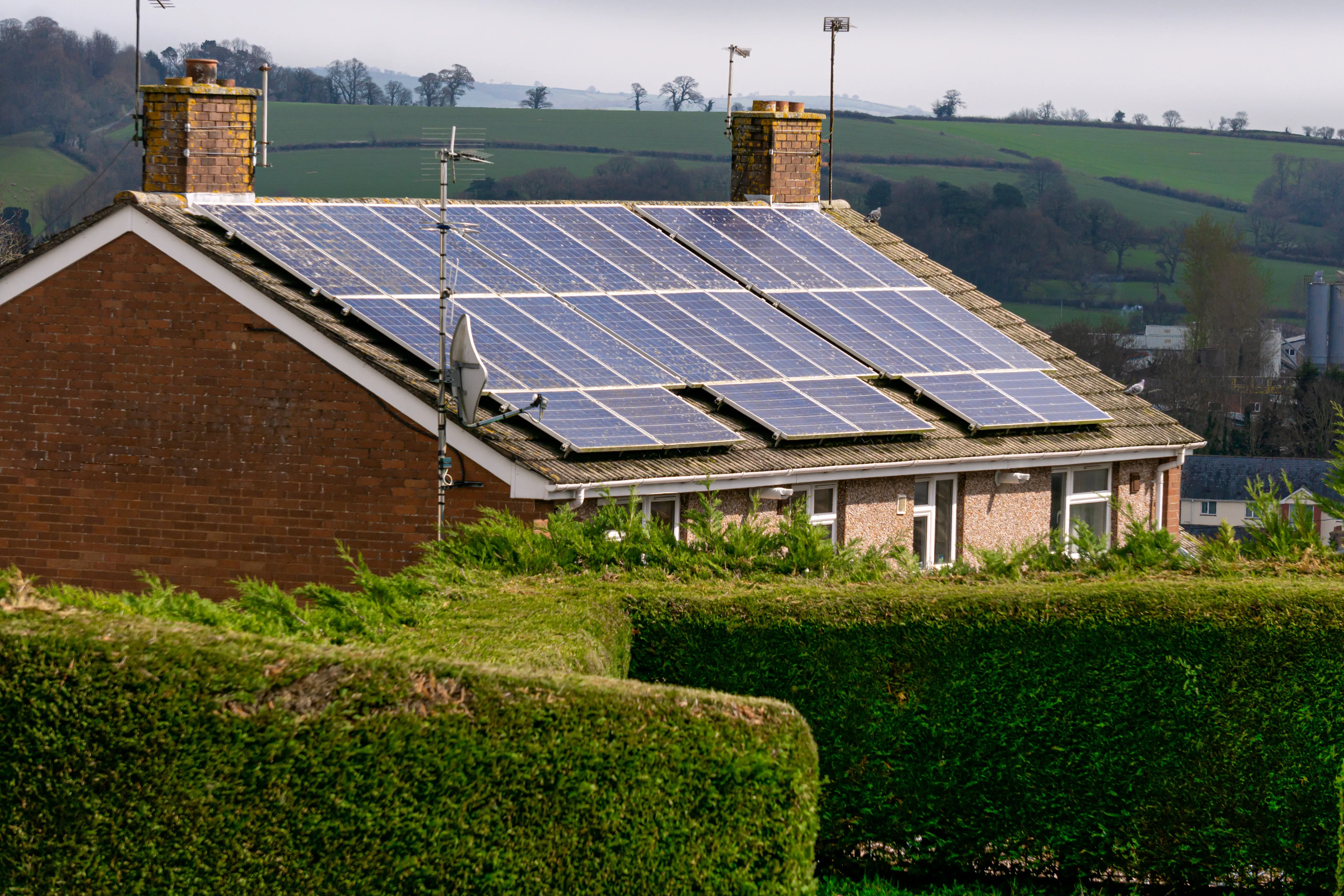 Brick house with solar panels on roof overlooking green fields.