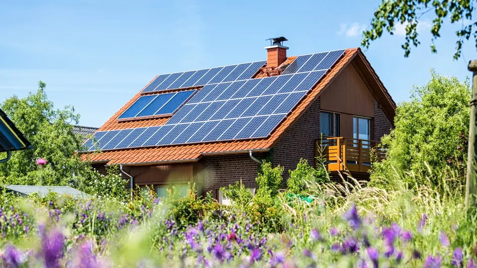 Ett tegelhus med solceller på taket och lila blommor i förgrunden.
