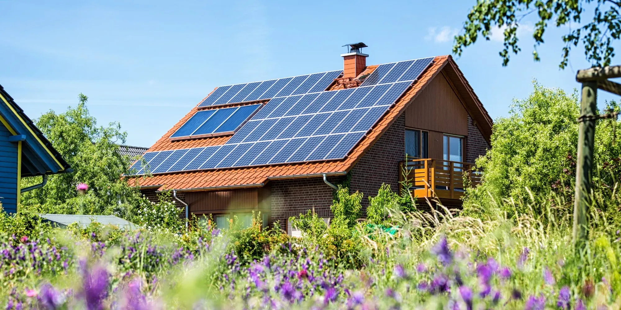 Ett tegelhus med solceller på taket och lila blommor i förgrunden.