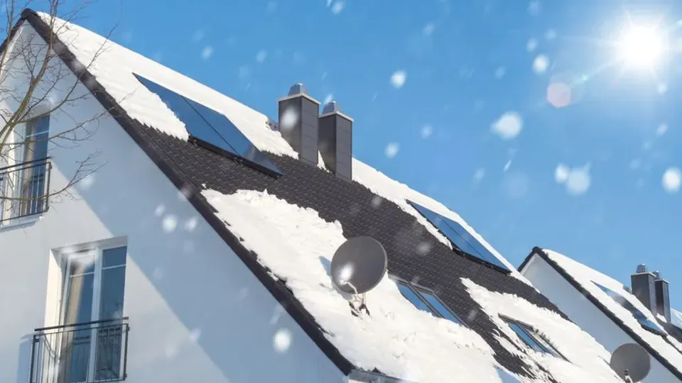 Solceller på ett snöigt tak med blå himmel i bakgrunden.