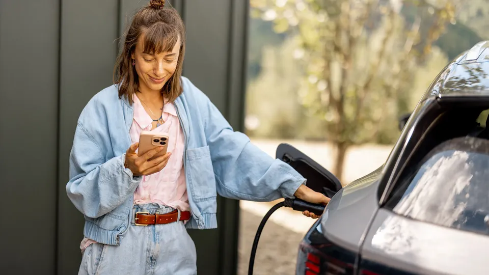 Kvinde holder smartphone mens hun oplader elektrisk bil.