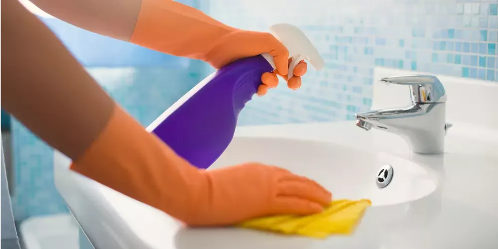 Person med orange städhandskar sprayar rengöringsmedel i ett handfat.