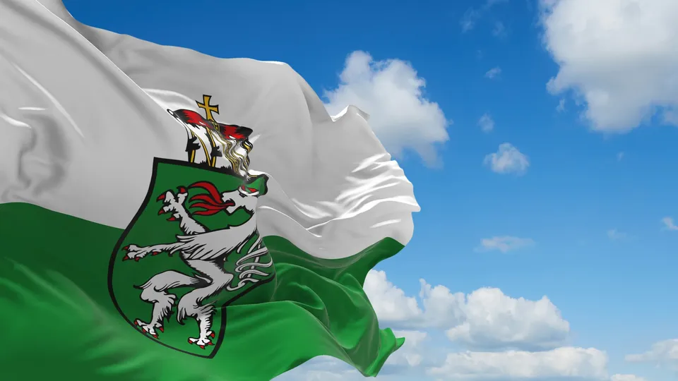 Grün-weiße Flagge der Steiermark mit dem steirischen Wappen vor blauem Himmel mit Wolken.
