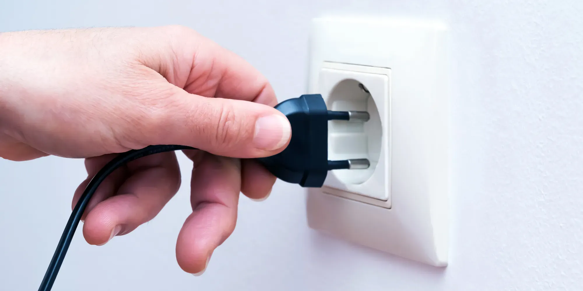 Hand inserting blue electrical plug into white wall outlet.