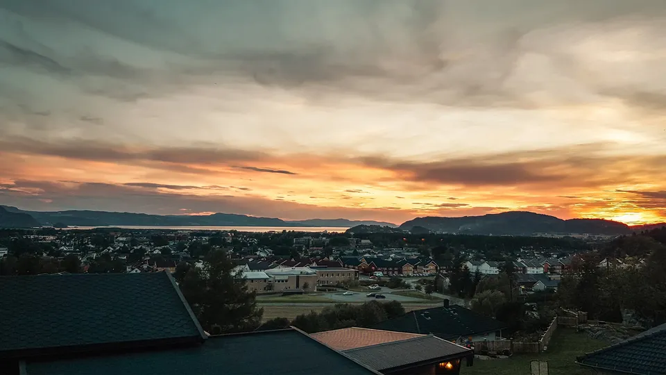Solnedgang over boligby med tak og fjord i fjerne.