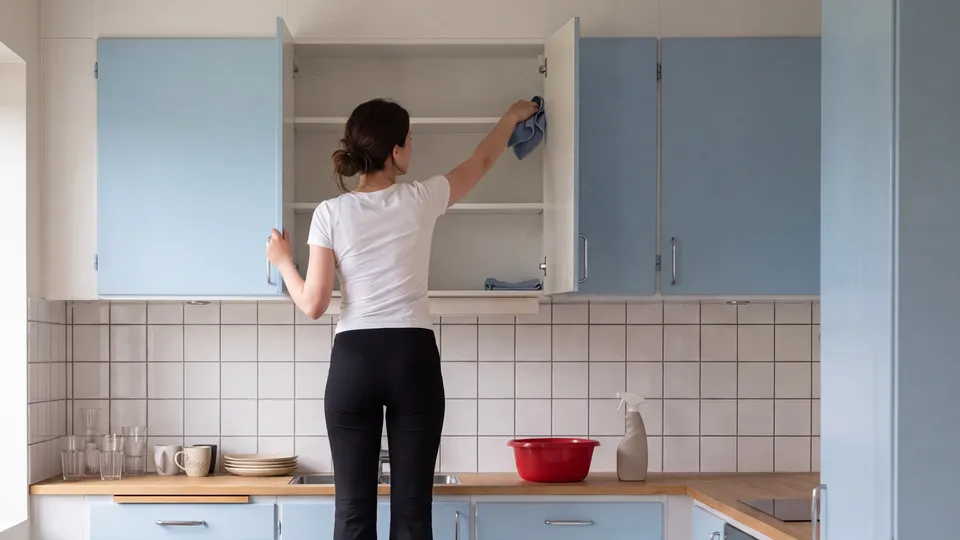 Kvinna sträcker sig in i öppet köksskåp för att torka inuti köksskåpet.