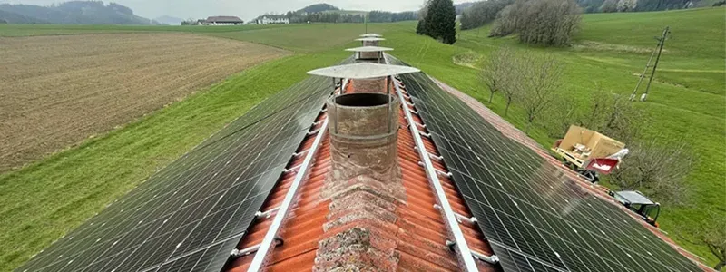 S-Tron GmbH – Luftaufnahme eines Bauernhausdachs mit beidseitig verlegter Photovoltaikanlage inmitten grüner Felder