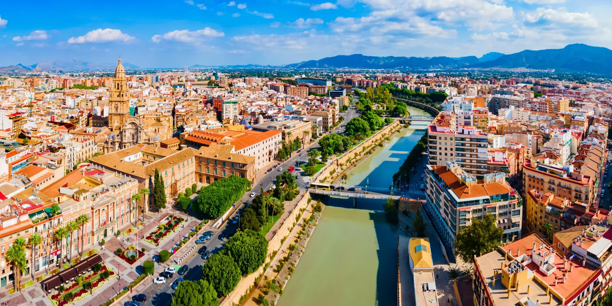 Vista aérea del paisaje urbano de Murcia con catedral, río y montañas.