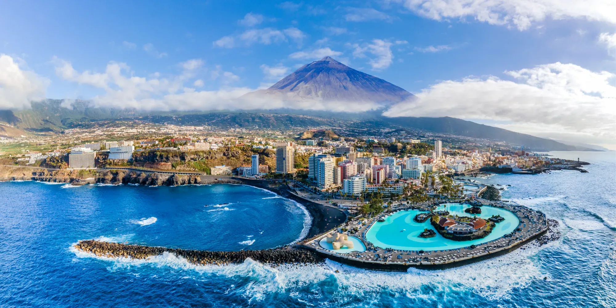 Ciudad costera con volcán y complejo de piscina turquesa.