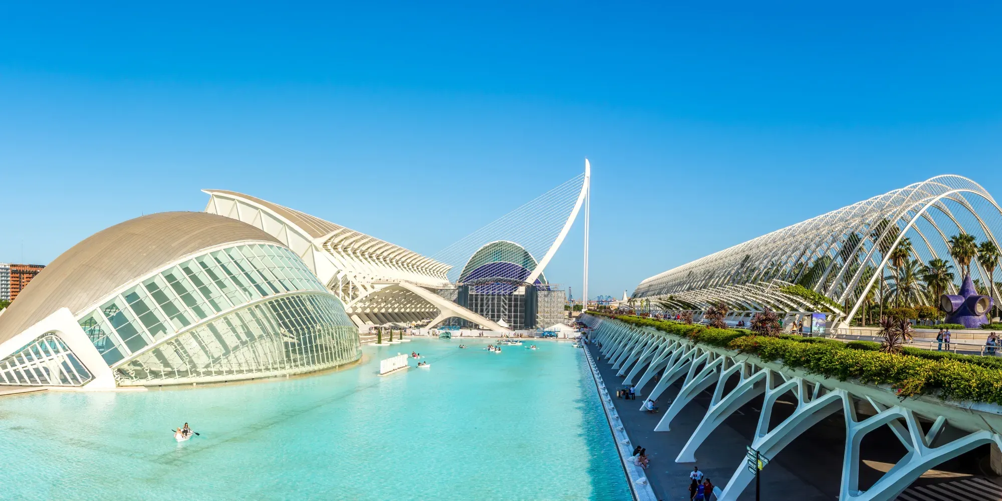 Estructuras arquitectónicas blancas modernas rodeando agua turquesa con palmeras y cielo azul despejado.