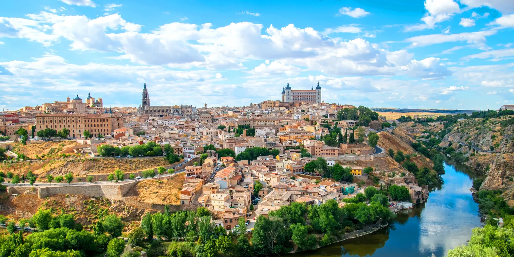 Ciudad histórica en colina con catedral y castillo sobre valle fluvial.