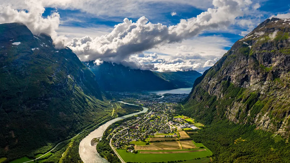 Luftfoto av en dal med en slingrende elv, jordbruksland og en by omgitt av bratte fjell.