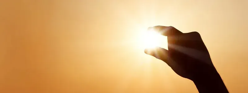 La sagoma di una mano contro un sole luminoso in un cielo arancione, come se pizzicasse il sole tra due dita.