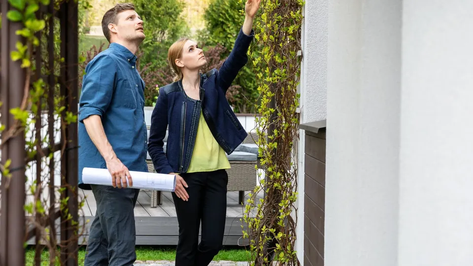 Takstperson og boligeier inspiserer boligens fasade i forbindelse med en boligsalgsrapport.