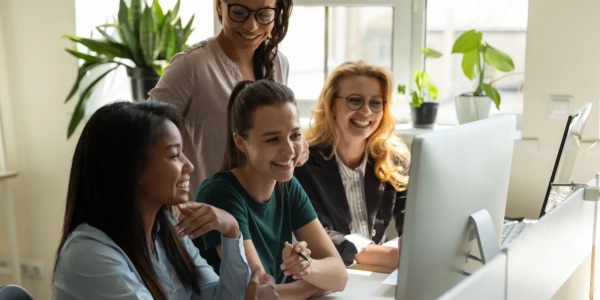 Cuatro mujeres sonriendo mientras miran pantallas de computadora en una oficina.